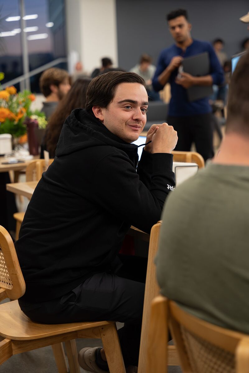 A teammate smiling over his shoulder at a busy café table
