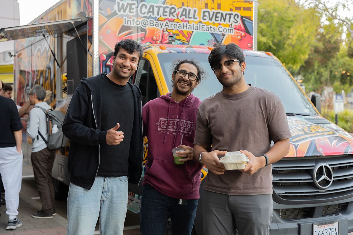 Three teammates smiling with lunch in front of a colorful food truck