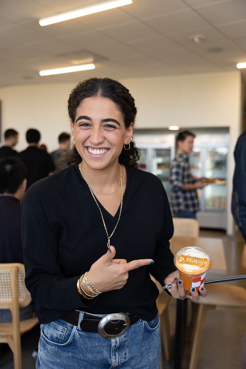 A teammate smiling and holding a Replit-branded drink at a team event