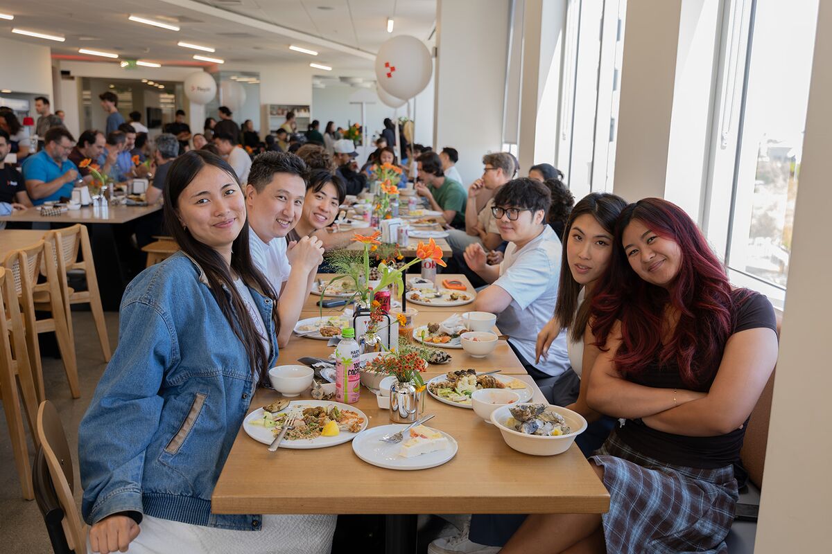 Teammates smiling for the camera at a long, busy lunch table