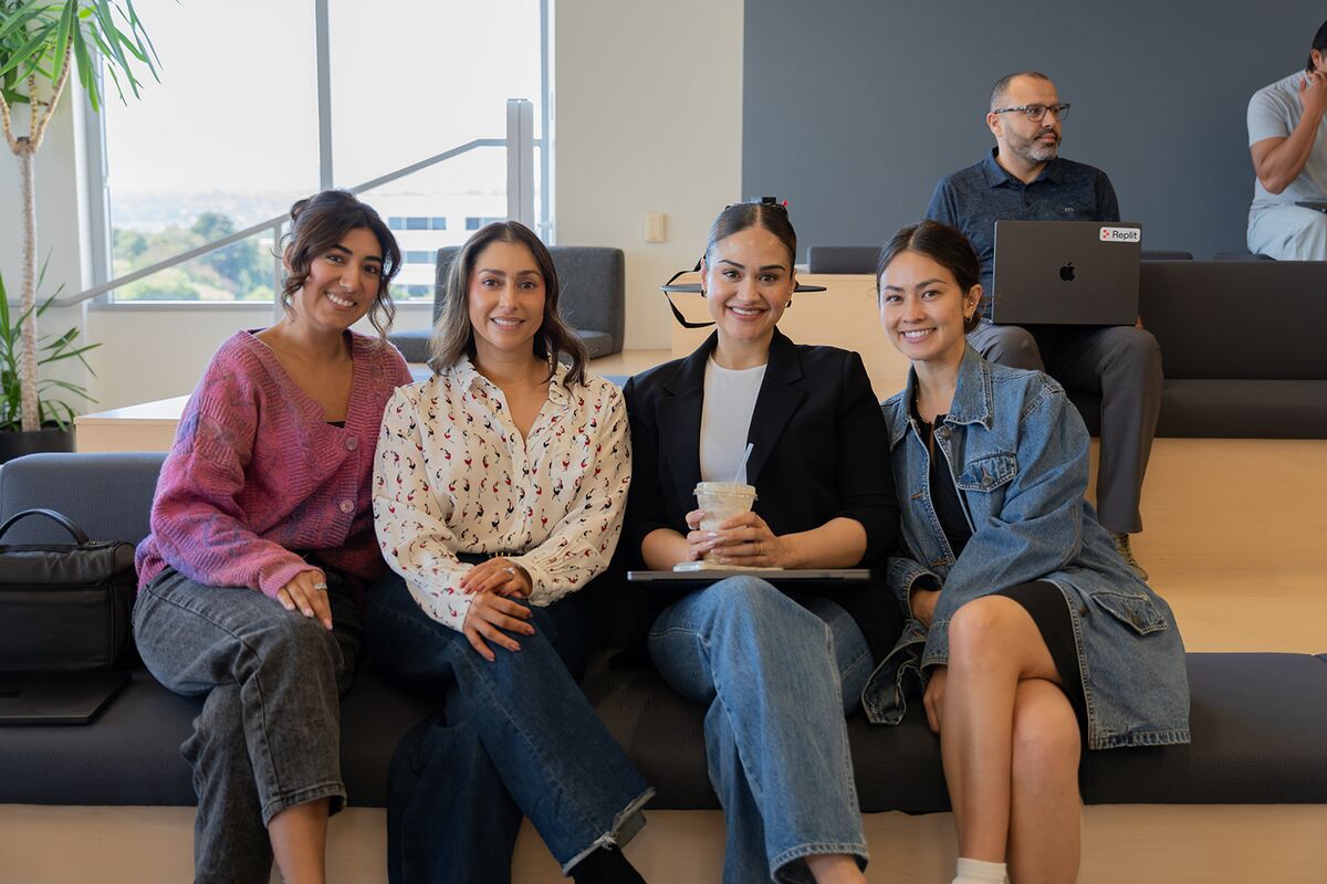 Four teammates smiling together on a lounge sofa at the office