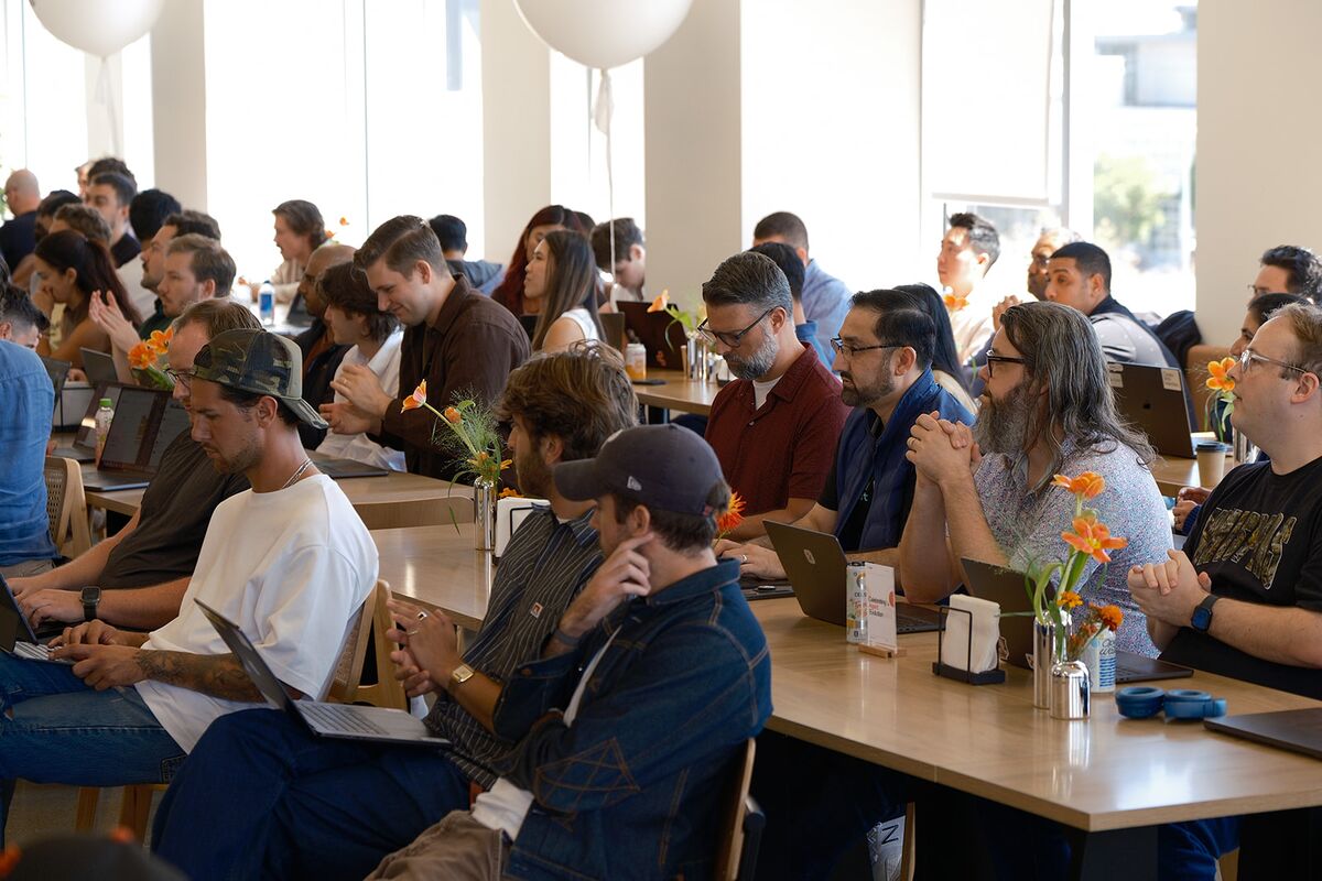 A bright, open workspace filled with teammates working at long tables