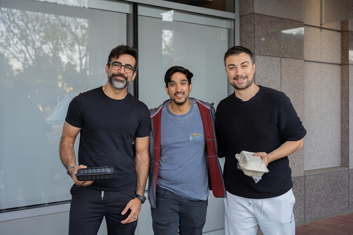 Three teammates posing arm in arm outside the office