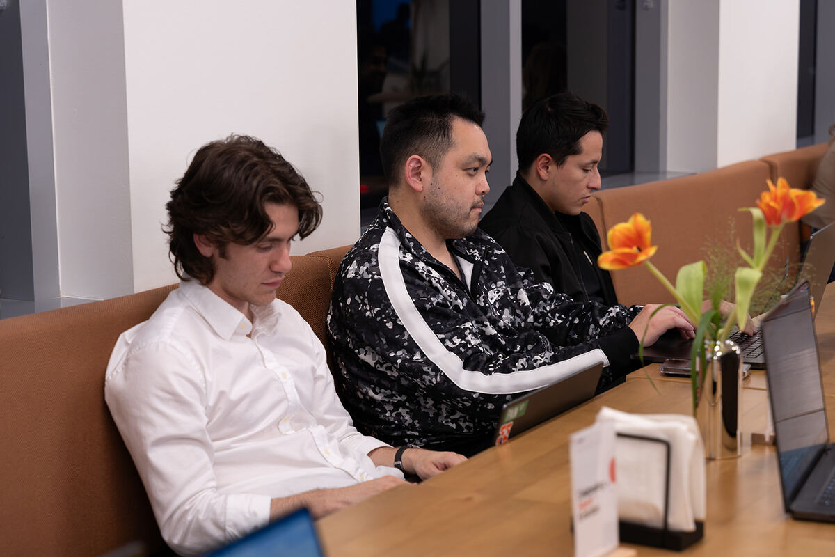 Three teammates working on laptops side by side at a café table with orange flowers