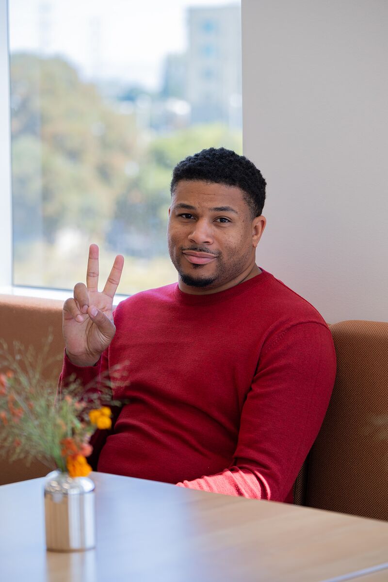 A teammate smiling and flashing a peace sign by a sunny window