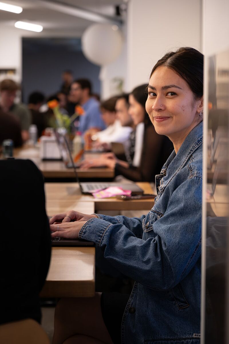 A teammate smiling over at the camera from a busy shared workspace